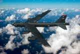 A B-52 bomber flies over clouds.